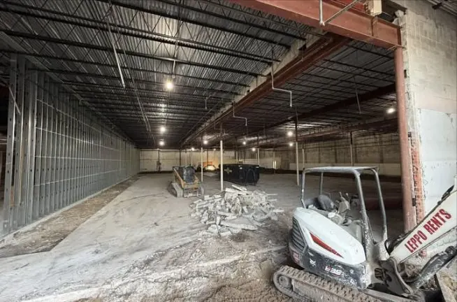 Long empty interior with a mini excavator and a pile of broken concrete